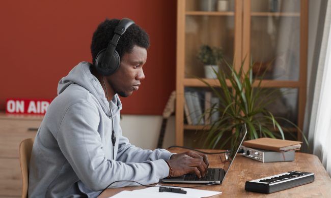 Side view portrait of young African-American musician using laptop while composing music at home, copy space